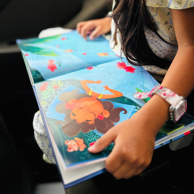 Fotografía compartida por un cliente que muestra a una niña pequeña muy entretenida leyendo el interior del libro "Don Coquí y la Noche Silenciosa" mientras viaja en el asiento trasero de un auto.