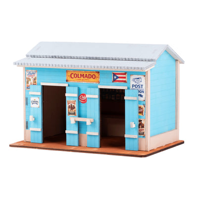 Fotografía de estudio de El Colmado pintado en color turquesa con letrero "Colmado" y stickers vintage aplicados, mostrando el resultado final de la manualidad de madera.