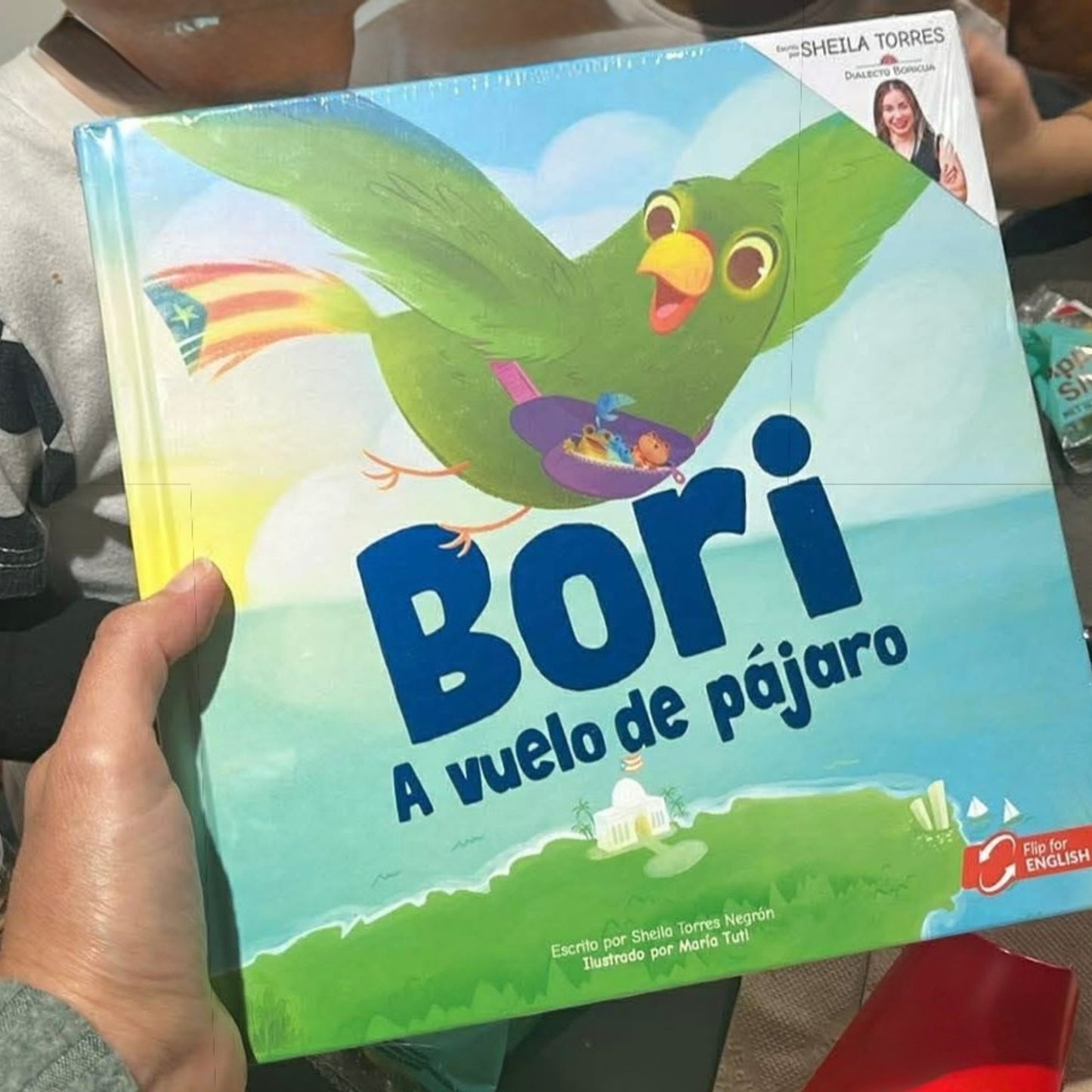 Fotografía compartida por un cliente sosteniendo en sus manos el libro "Bori: A Vuelo de Pájaro", mostrando el tamaño real del producto y los colores vibrantes de su portada.