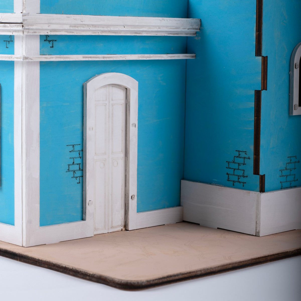 Fotografía de estudio de un acercamiento al interior pintado de El Faro Los Morrillos, mostrando la puerta blanca, el rodapié y el detalle de ladrillos en la pared turquesa.