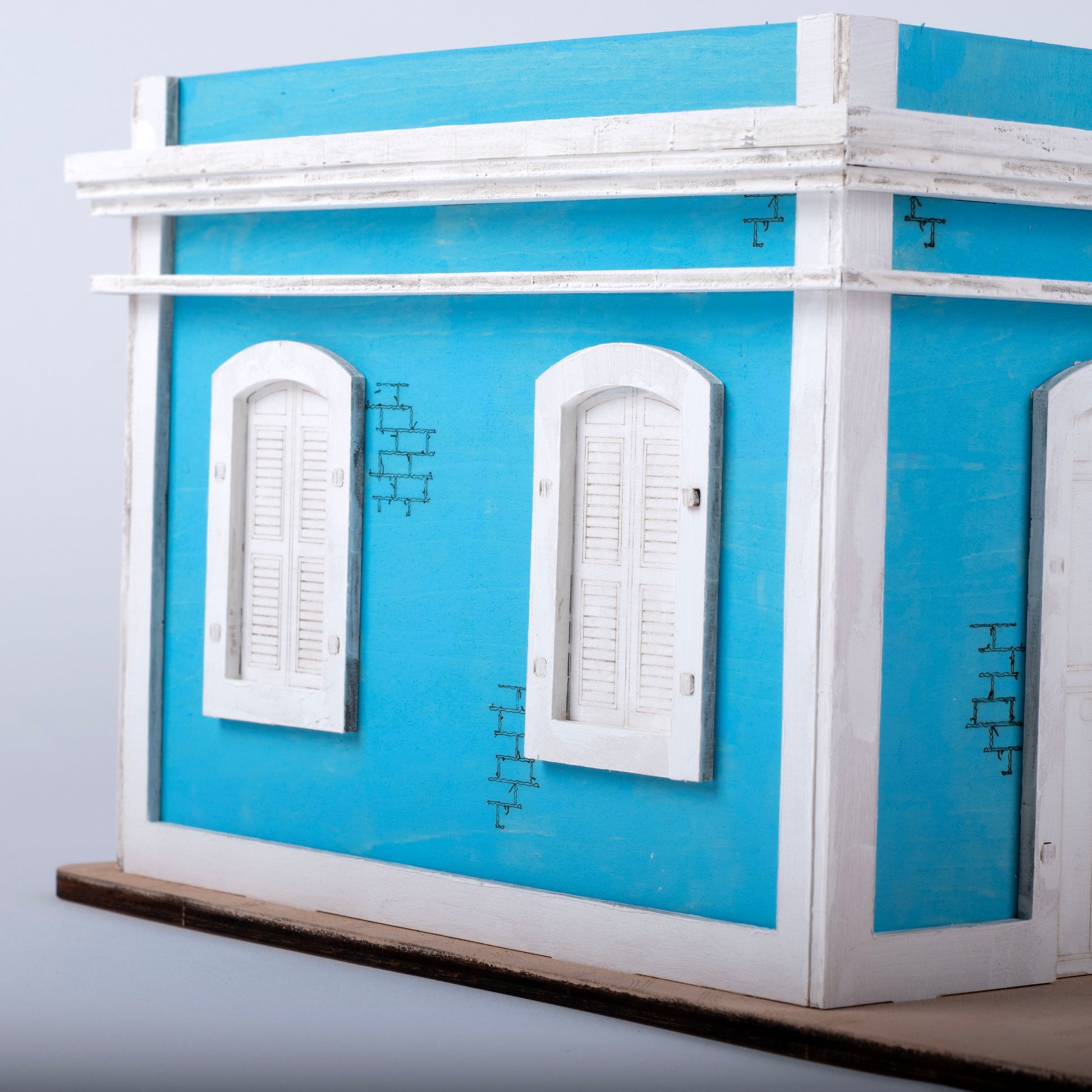 Fotografía de estudio de un acercamiento a la fachada pintada en turquesa de El Faro Los Morrillos, mostrando el detalle de las ventanas con persianas blancas y los ladrillos ilustrados.