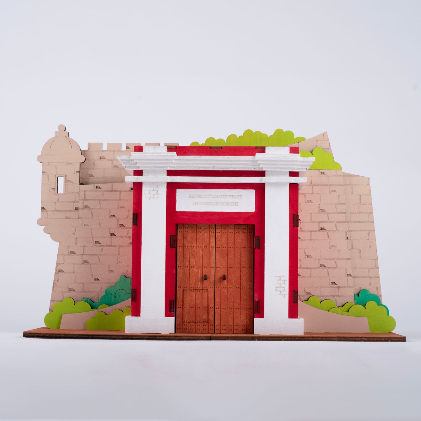 Fotografía de estudio de La Puerta de San Juan pintada en rojo, blanco y beige, mostrando la garita, el arco central y la inscripción "Benedictus qui venit in nomine Domini".