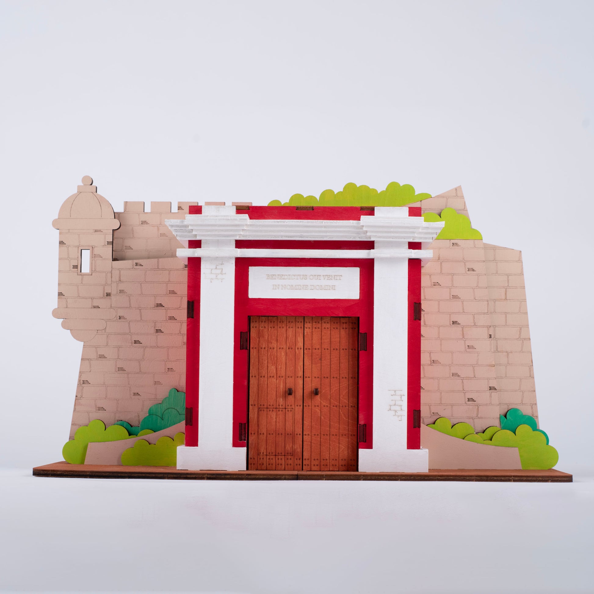 Fotografía de estudio de La Puerta de San Juan pintada en rojo, blanco y beige, mostrando la garita, el arco central y la inscripción "Benedictus qui venit in nomine Domini".