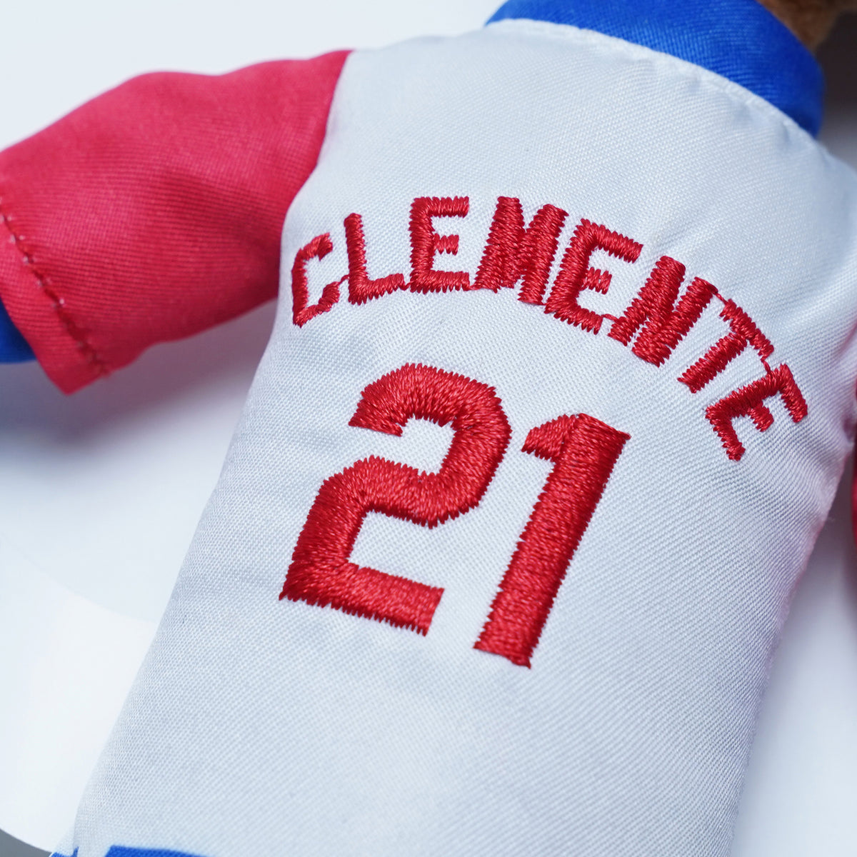 Fotografía de estudio de un acercamiento a la espalda del uniforme del peluche, con CLEMENTE y el número 21 bordados en rojo.