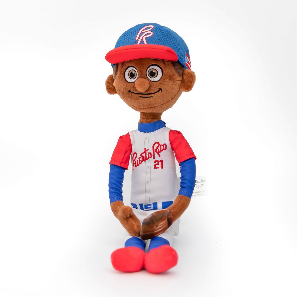 Fotografía de estudio del peluche de Clemente sentado, con uniforme de Puerto Rico #21, gorra azul con visera roja y guante de béisbol en la mano.